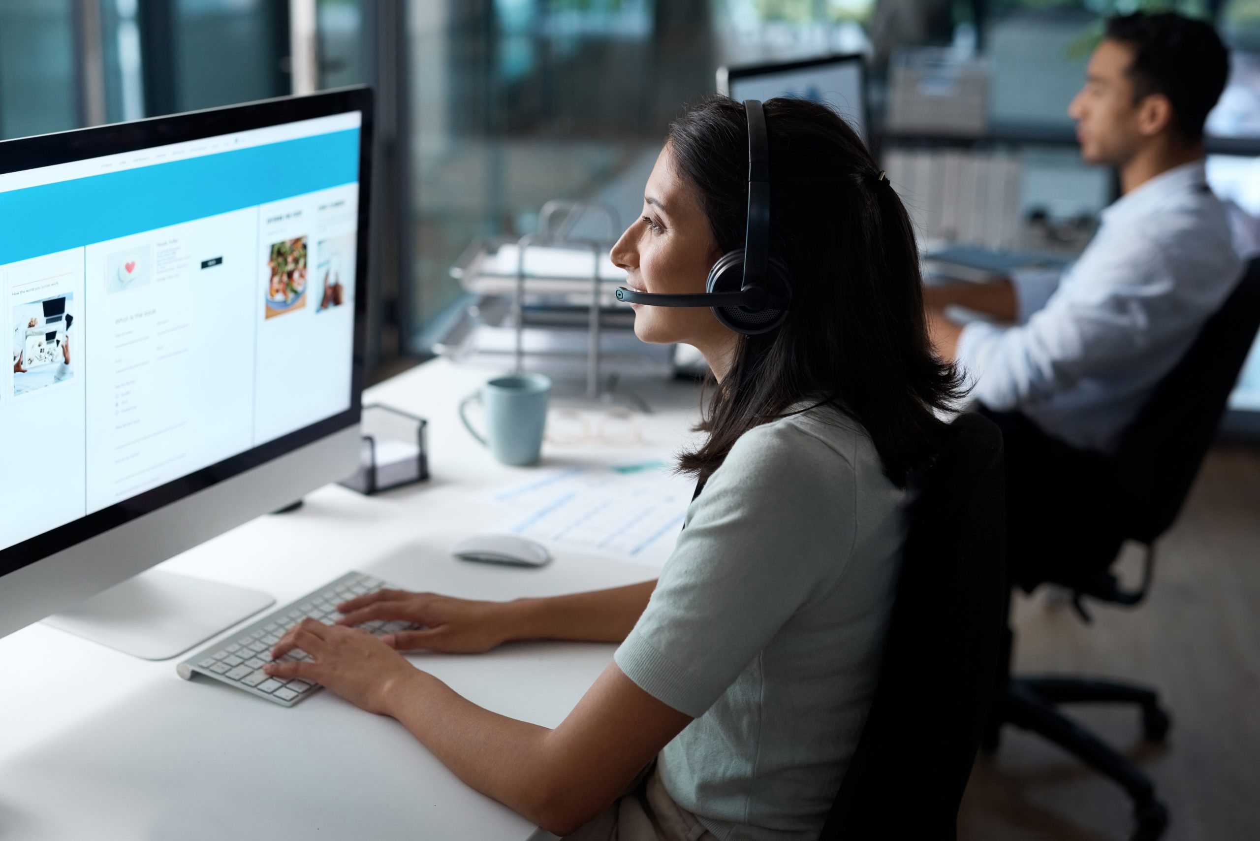 Shot of a young woman using a headset and computer in a modern office.